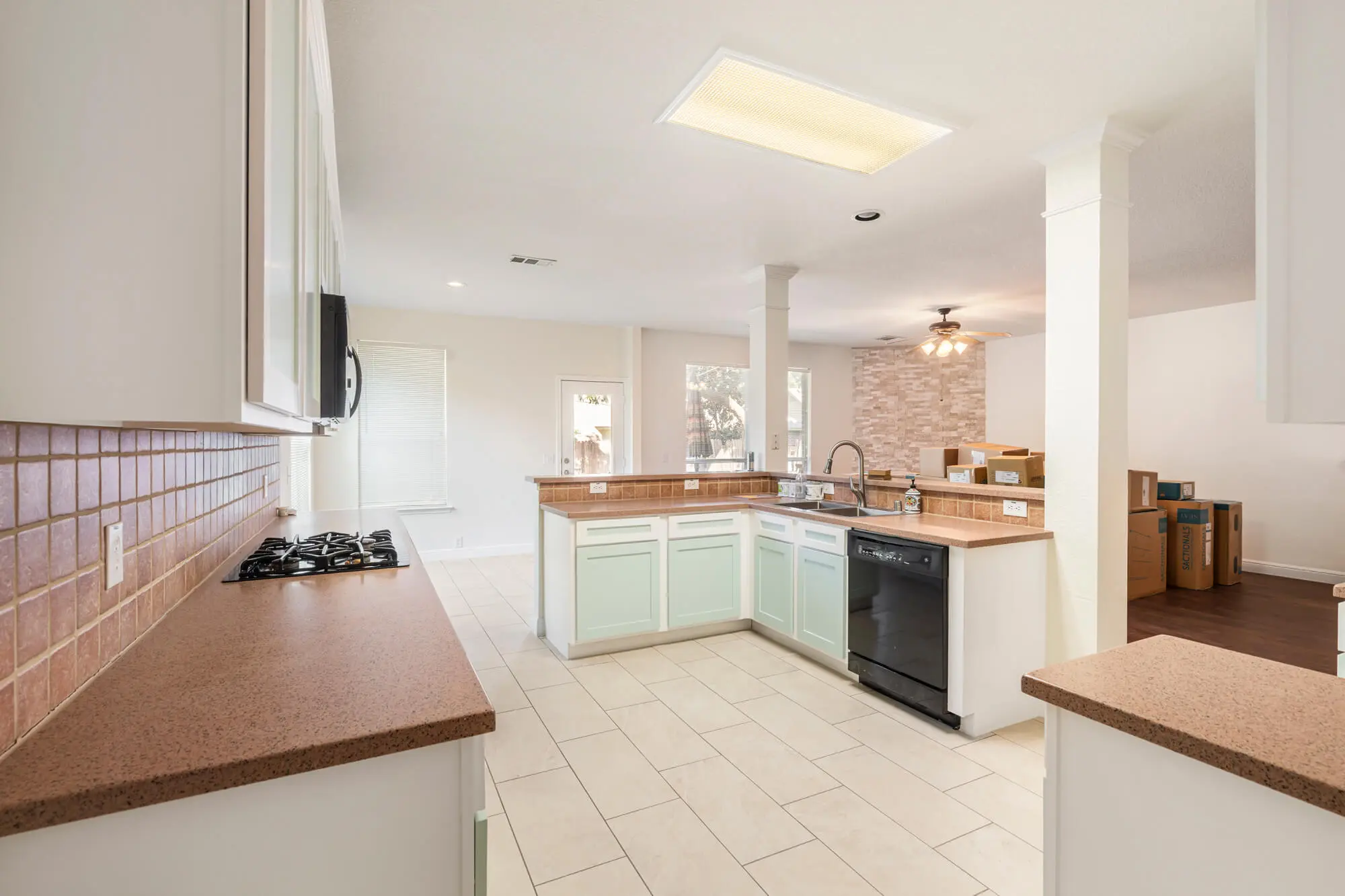 Wide angle kitchen view showing freshly refinished white upper cabinets and mint green lower cabinets with gas cooktop and open sightlines to the living area on a cabinet refinishing Fort Worth project by J&R Alliance Painting LLC