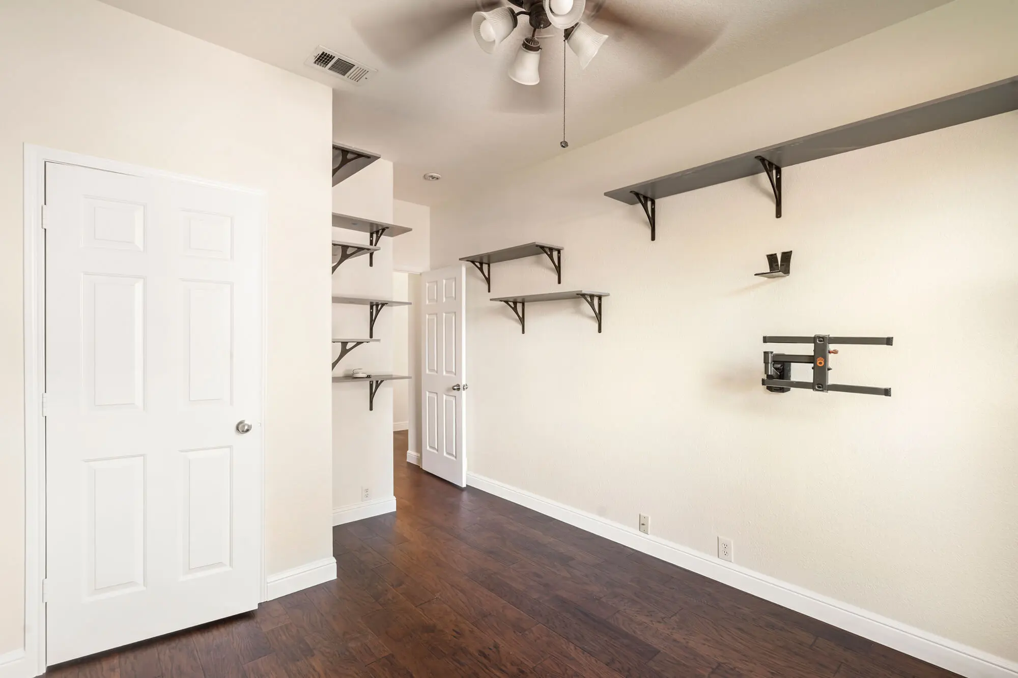 Freshly painted cream bedroom with white doors, white baseboards, dark hardwood floors, and wall mounted shelving completed on a DFW interior painting project by J&R Alliance Painting LLC