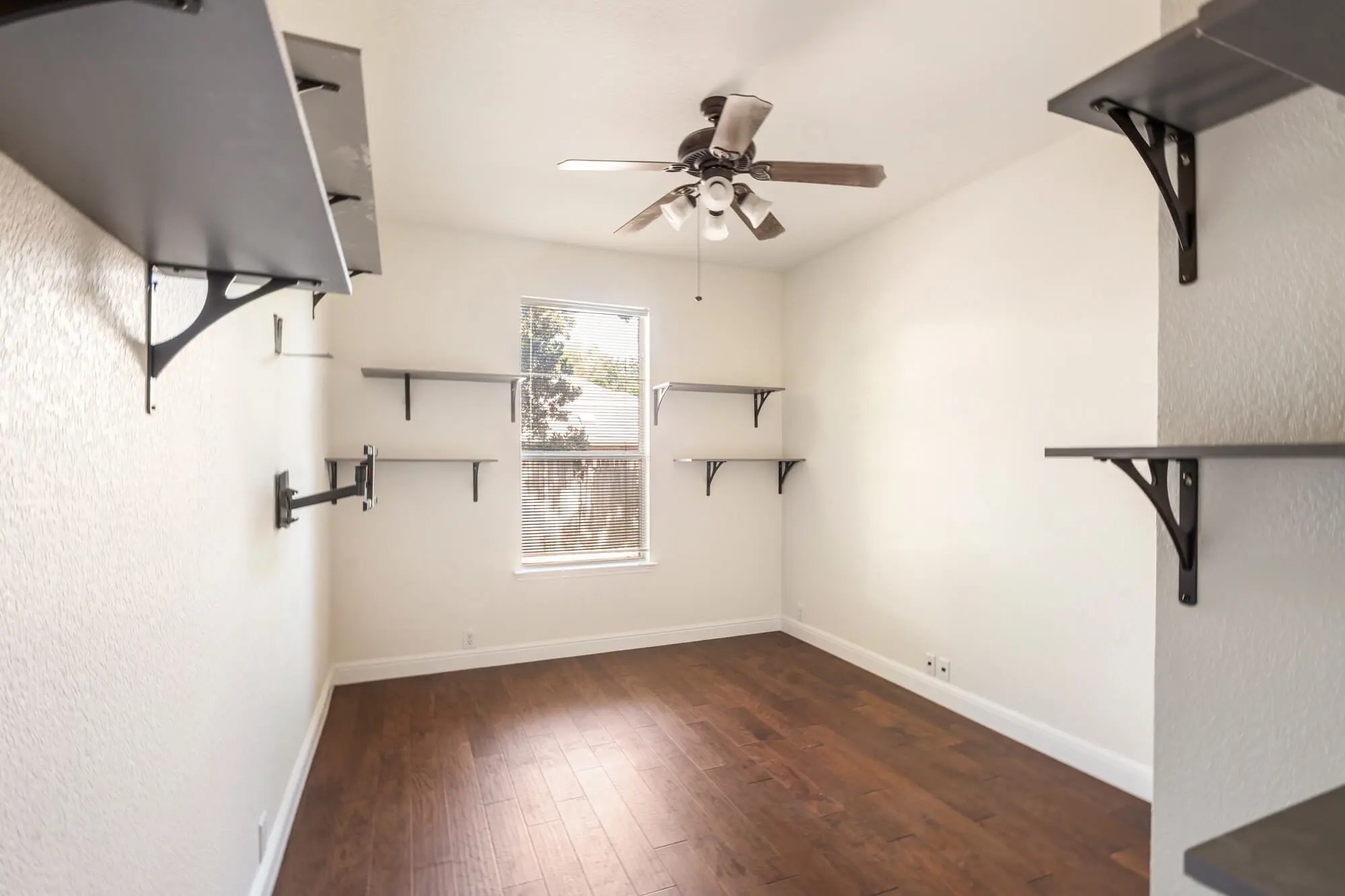 Freshly painted white bedroom with textured walls, white baseboards, dark hardwood floors, and wall mounted shelving on a DFW interior painting project by J&R Alliance Painting LLC