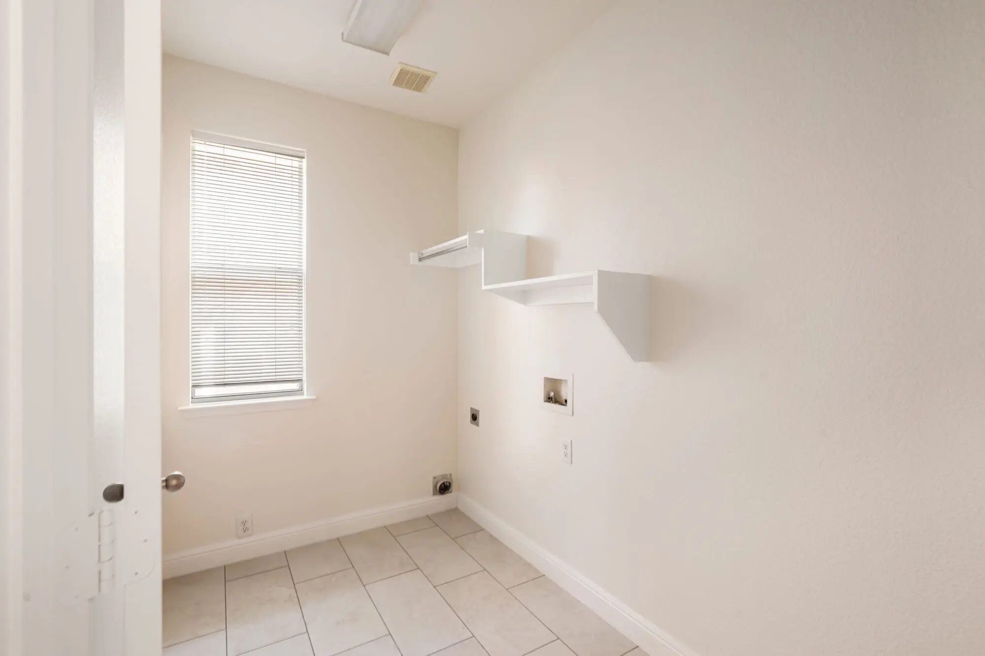 Freshly painted cream laundry room with white baseboards, white shelving, and tile floor on a DFW interior painting project by J&R Alliance Painting LLC