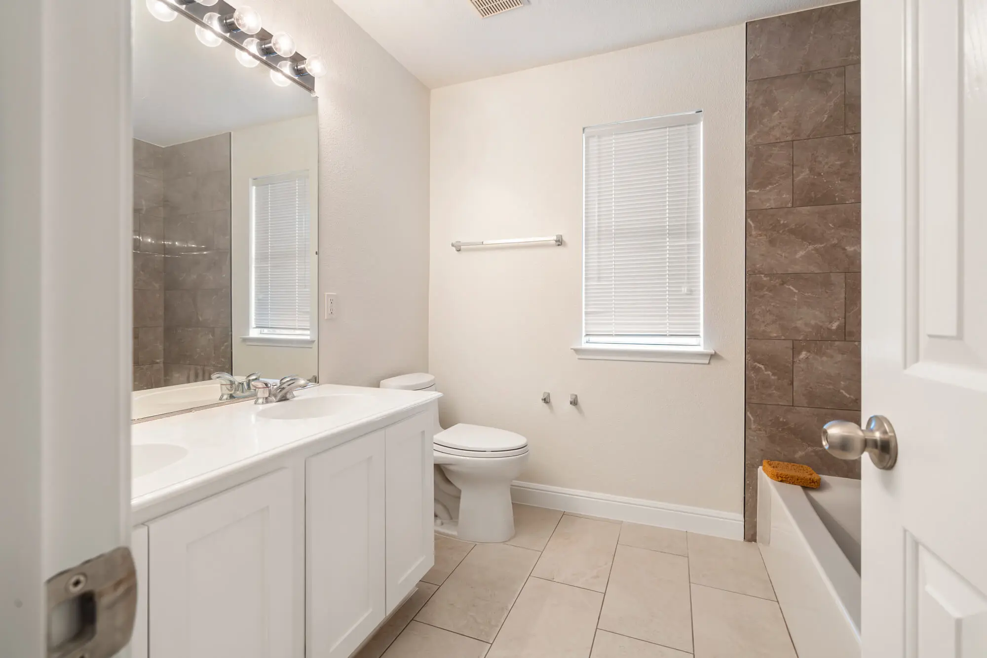Full bathroom with freshly painted cream walls, white shaker vanity cabinet, white baseboards, and large format tile tub surround on a DFW interior painting project by J&R Alliance Painting LLC