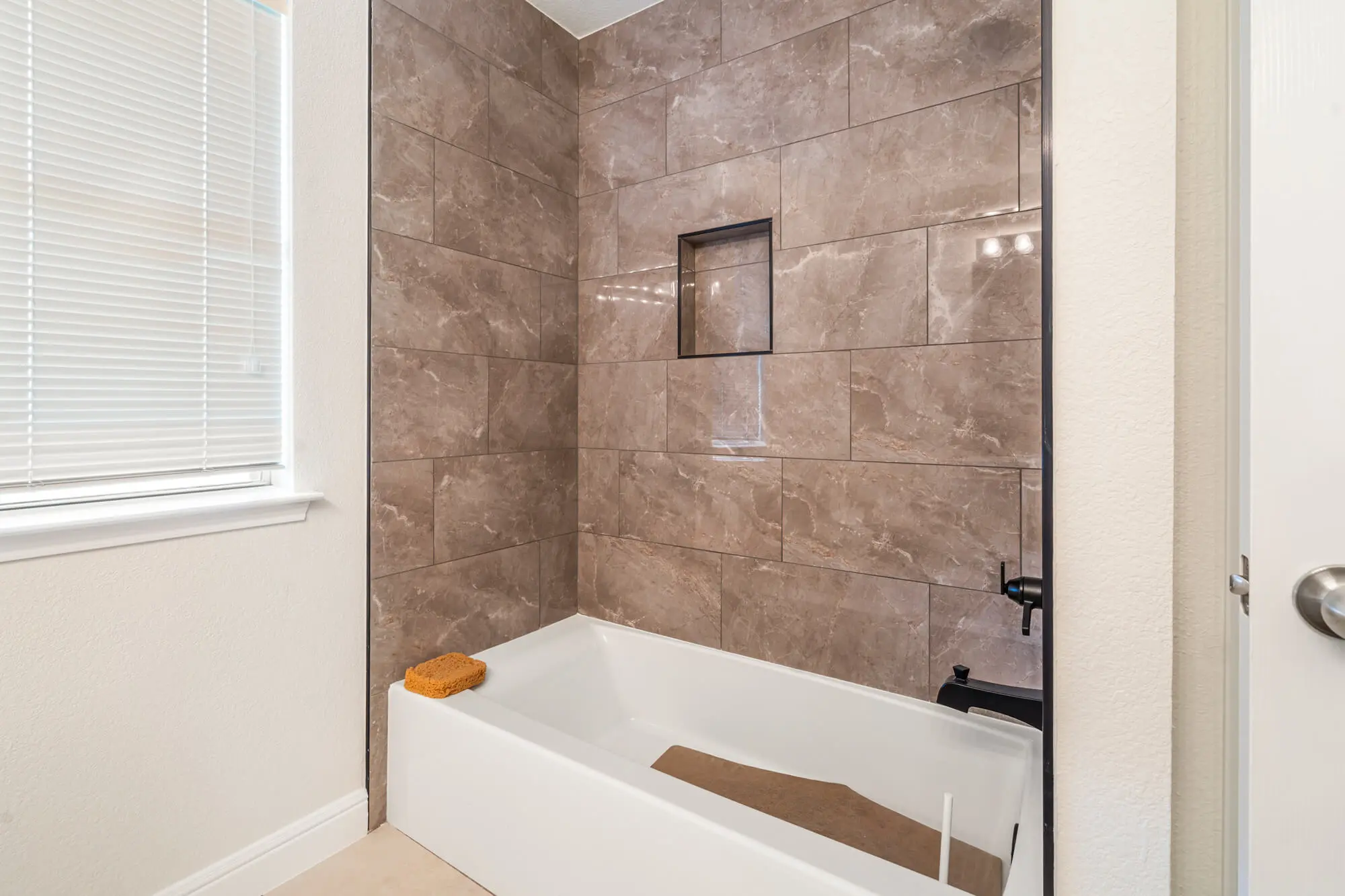 Freshly painted cream bathroom walls and white baseboards surrounding a tub shower combination with large format marble look tile on a DFW interior painting project by J&R Alliance Painting LLC