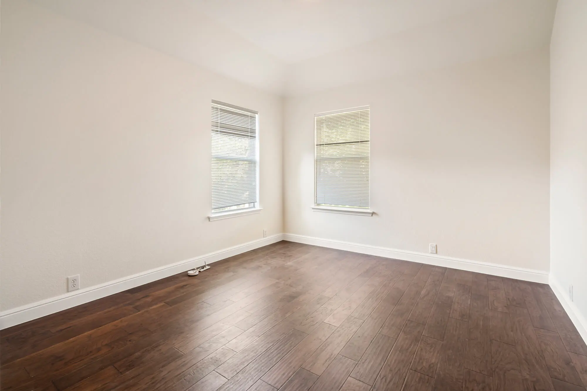 Corner bedroom with freshly painted warm white walls, clean white baseboards, dual windows, and dark hardwood floors on a DFW interior painting project by J&R Alliance Painting LLC