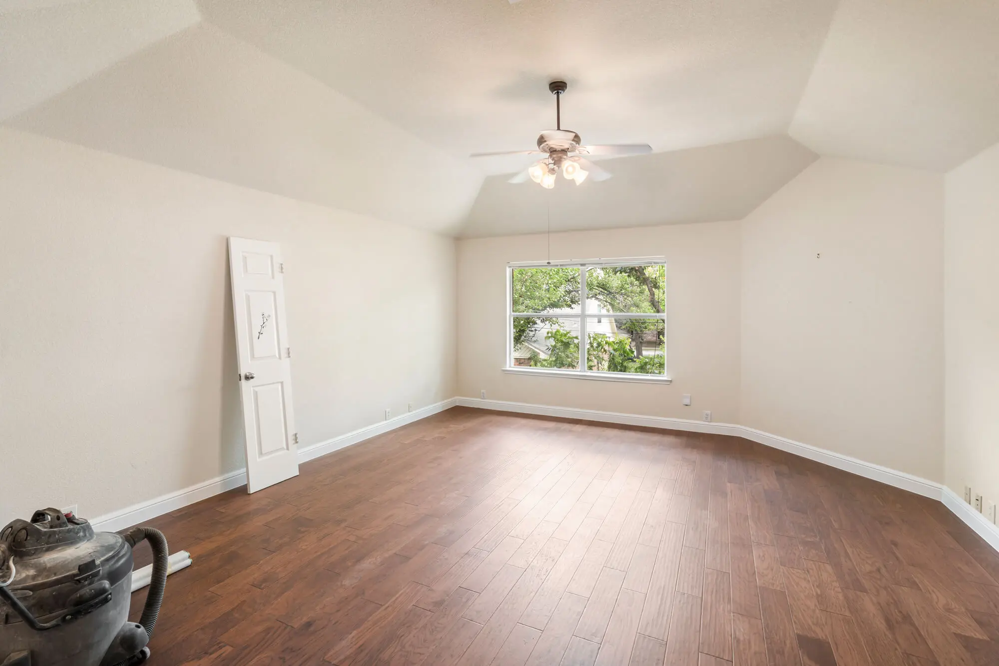 Freshly painted warm white bedroom with vaulted ceiling, hardwood floors, and clean white baseboards and trim during an interior painting Fort Worth project by J&R Alliance Painting LLC