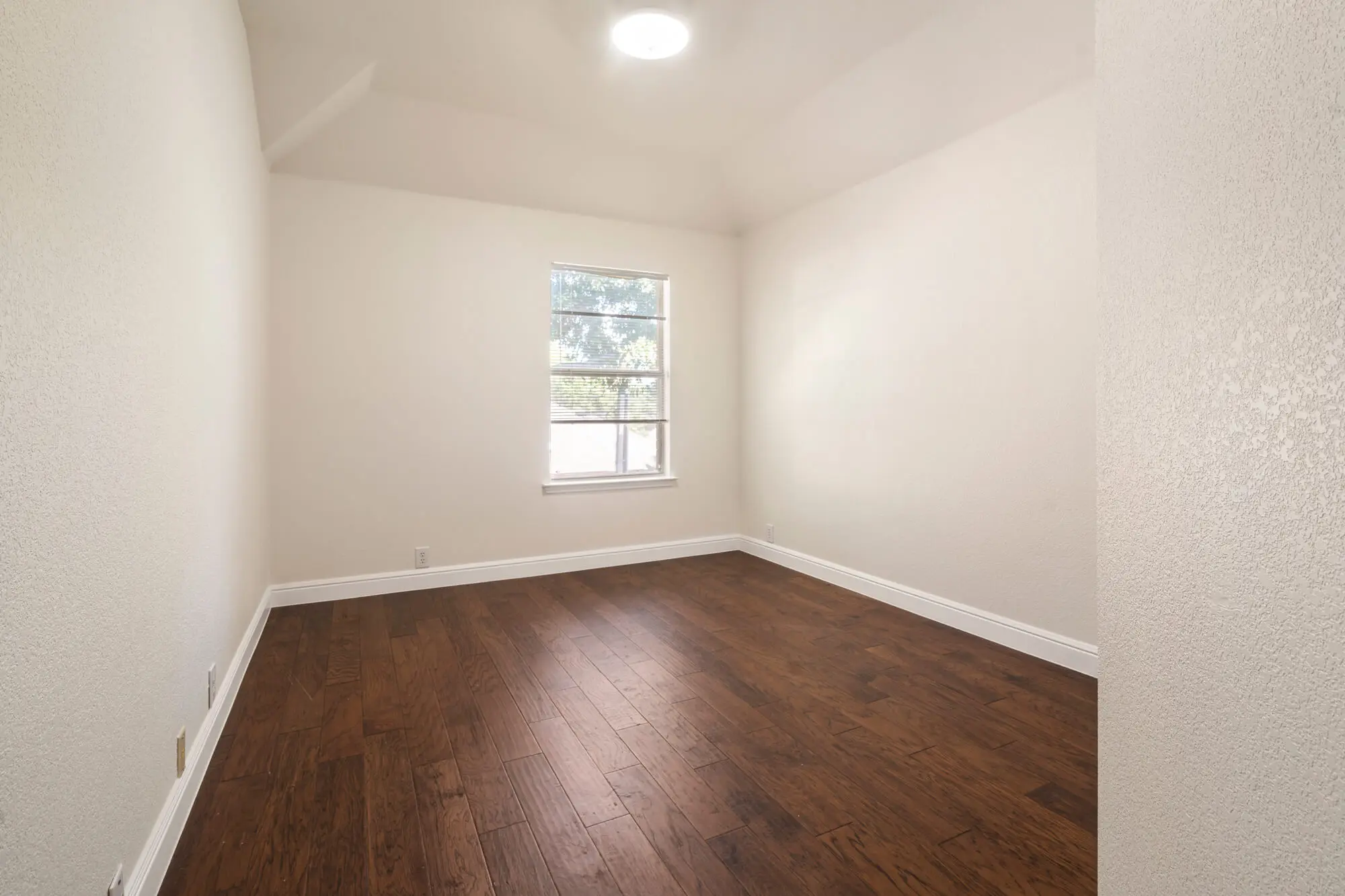 Clean white painted bedroom with textured walls, white baseboards, and dark hardwood floors after a DFW interior painting project by J&R Alliance Painting LLC