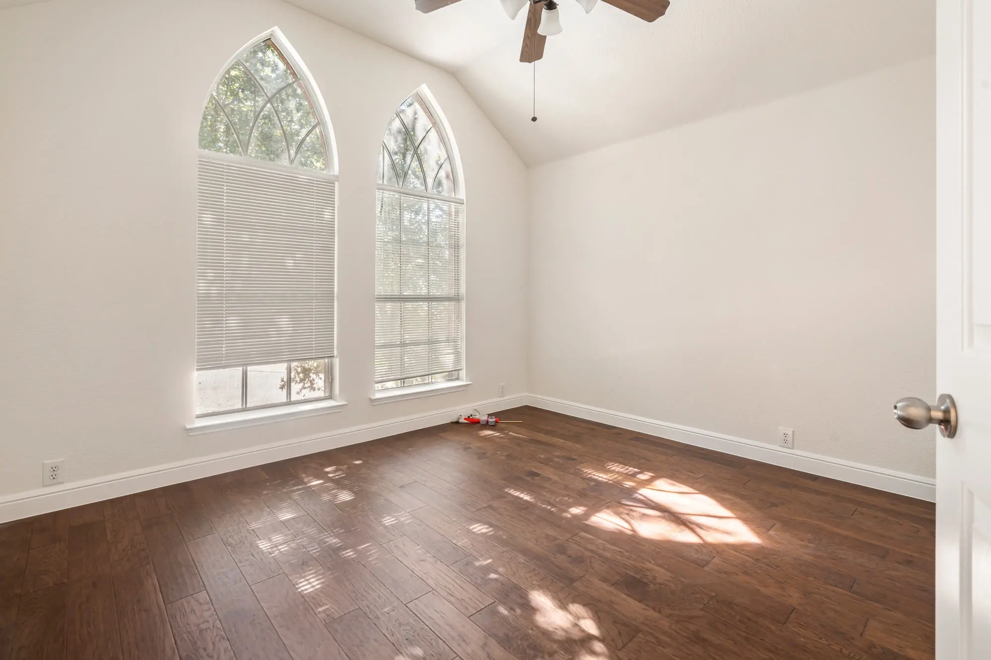 Bright room with freshly painted white walls and trim featuring cathedral arch windows, vaulted ceiling, and hardwood floors after an interior painting Fort Worth project by J&R Alliance Painting LLC
