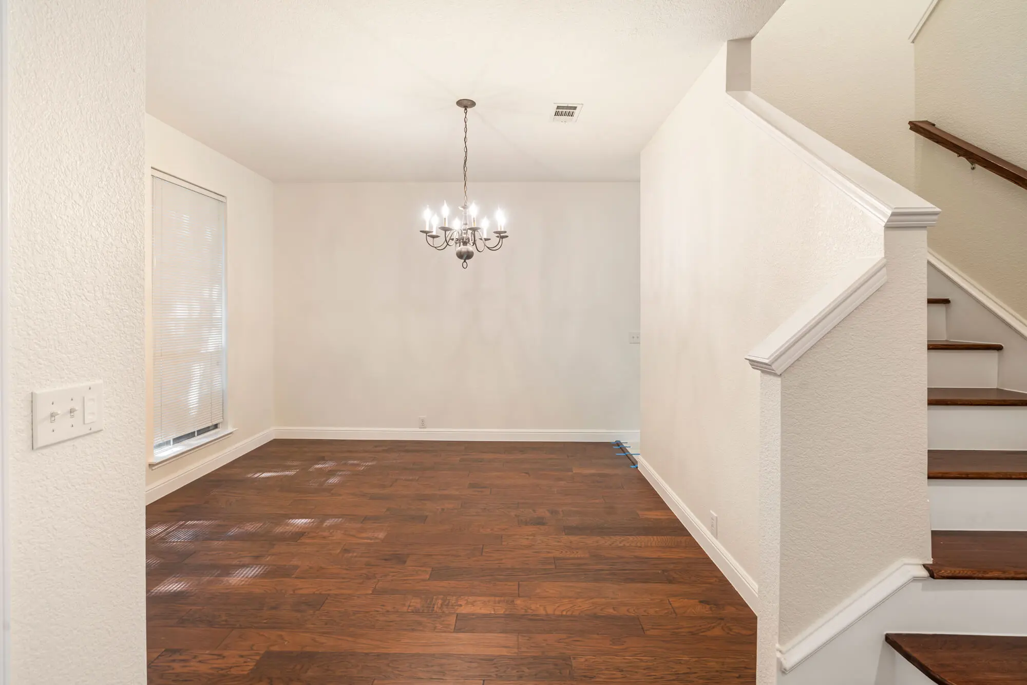 Dining room with freshly painted white walls and baseboards, chandelier, dark hardwood floors, and white painted staircase trim visible on a DFW interior painting project by J&R Alliance Painting LLC