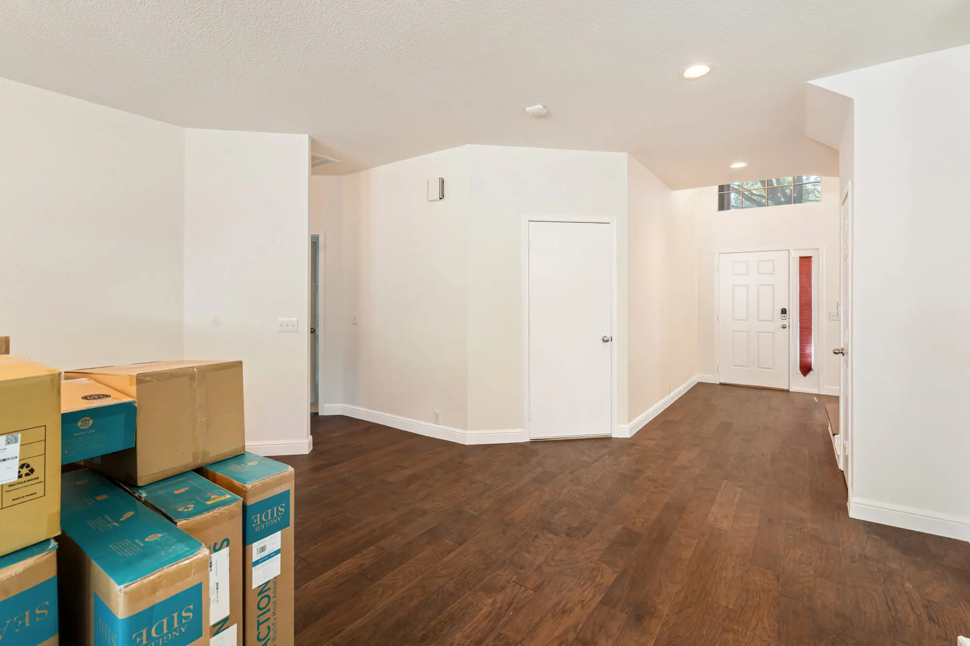 Open living area and entryway with freshly painted cream walls, white baseboards and doors, and dark hardwood floors on a DFW interior painting project by J&R Alliance Painting LLC