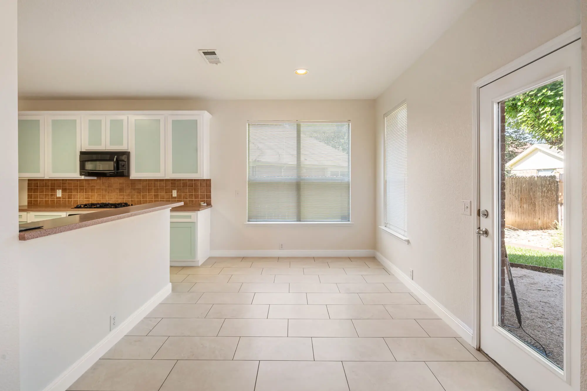 Breakfast nook and kitchen area with freshly painted cream walls, white baseboards, mint green and white refinished cabinets, and tile floors on a cabinet refinishing Fort Worth project by J&R Alliance Painting LLC