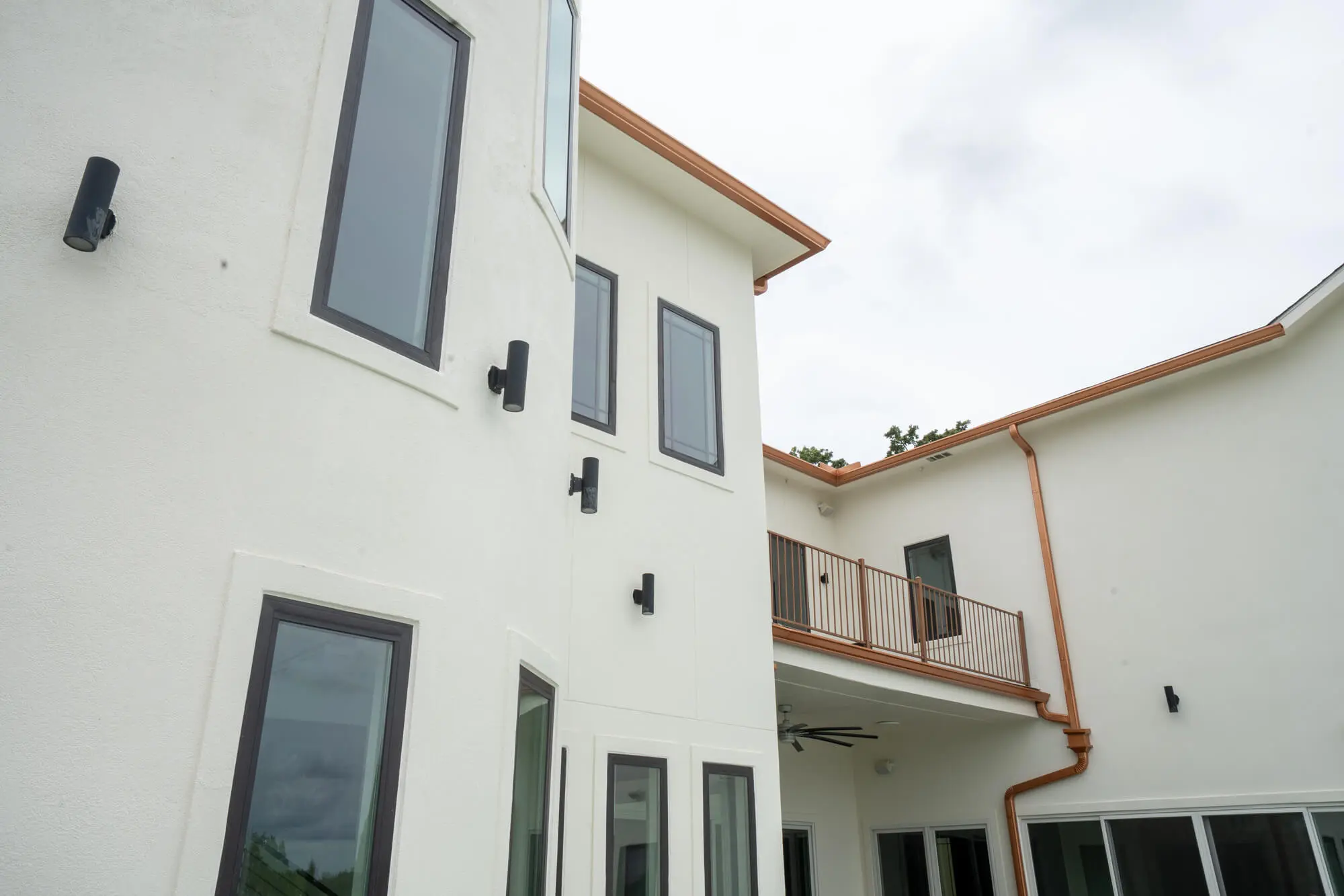 Rear elevation of a completed white stucco exterior repaint on a two story DFW custom home with charcoal window trim, copper gutters, and a second floor balcony