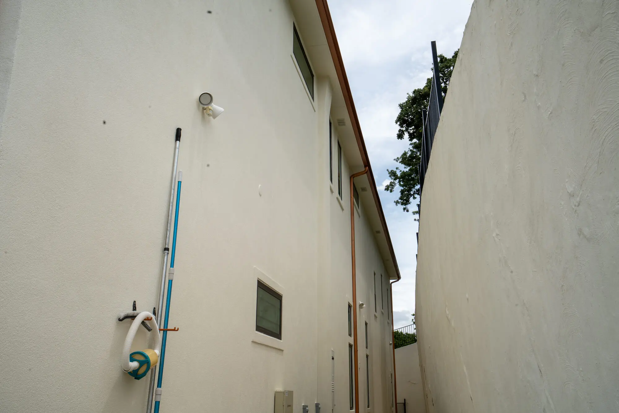 Side passageway between two freshly painted cream stucco exterior walls with painting equipment still on site during a DFW residential exterior project