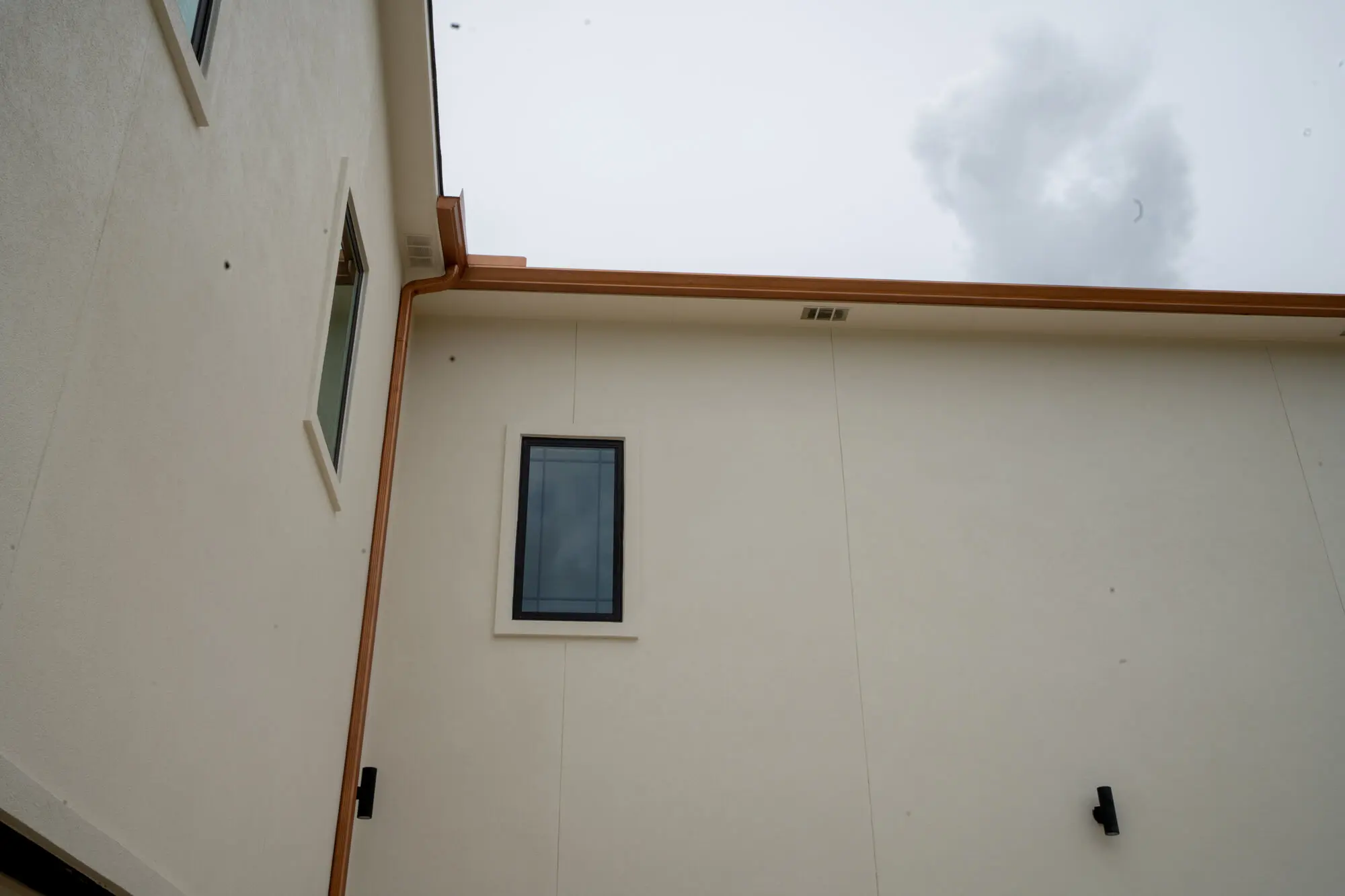 Close-up detail of clean cream stucco exterior finish at a roofline corner with copper gutters and crisp charcoal window trim on a DFW custom home