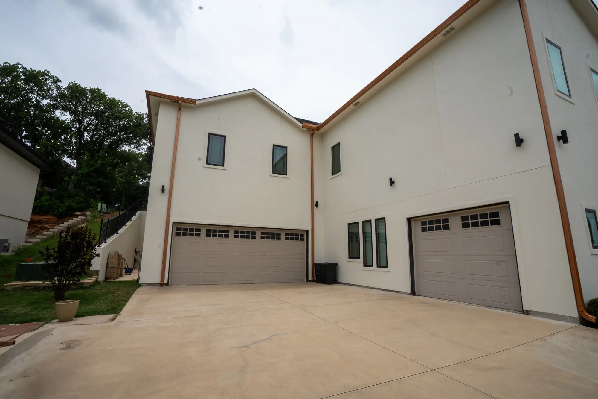 Side and garage elevation of a two story custom home with completed white stucco exterior repaint, copper gutters, and tan garage doors on a DFW residential property