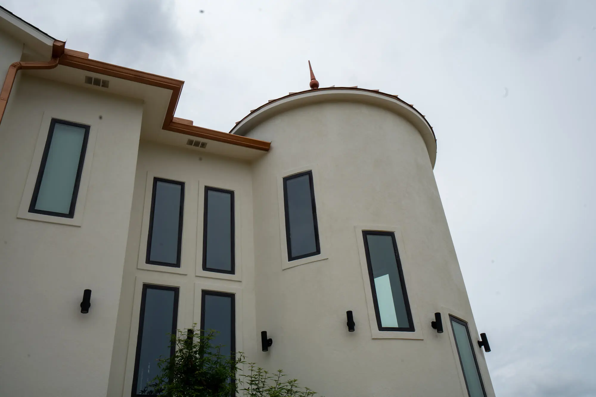 Cream stucco exterior repaint on a custom DFW home featuring a round turret tower with charcoal window trim and copper roofline details