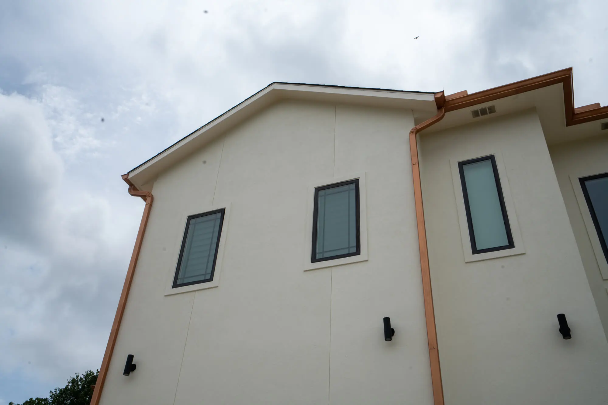 Close-up of a freshly painted cream stucco exterior upper elevation with charcoal window trim and copper gutters on a DFW residential home