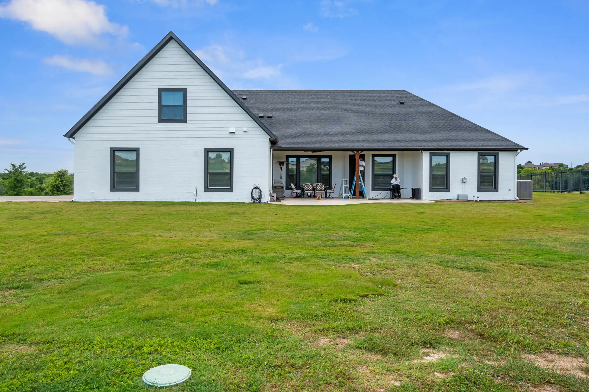 J&R Alliance Painting LLC crew finishing trim work on the covered porch of a white painted brick farmhouse with charcoal window trim during a DFW exterior repaint project