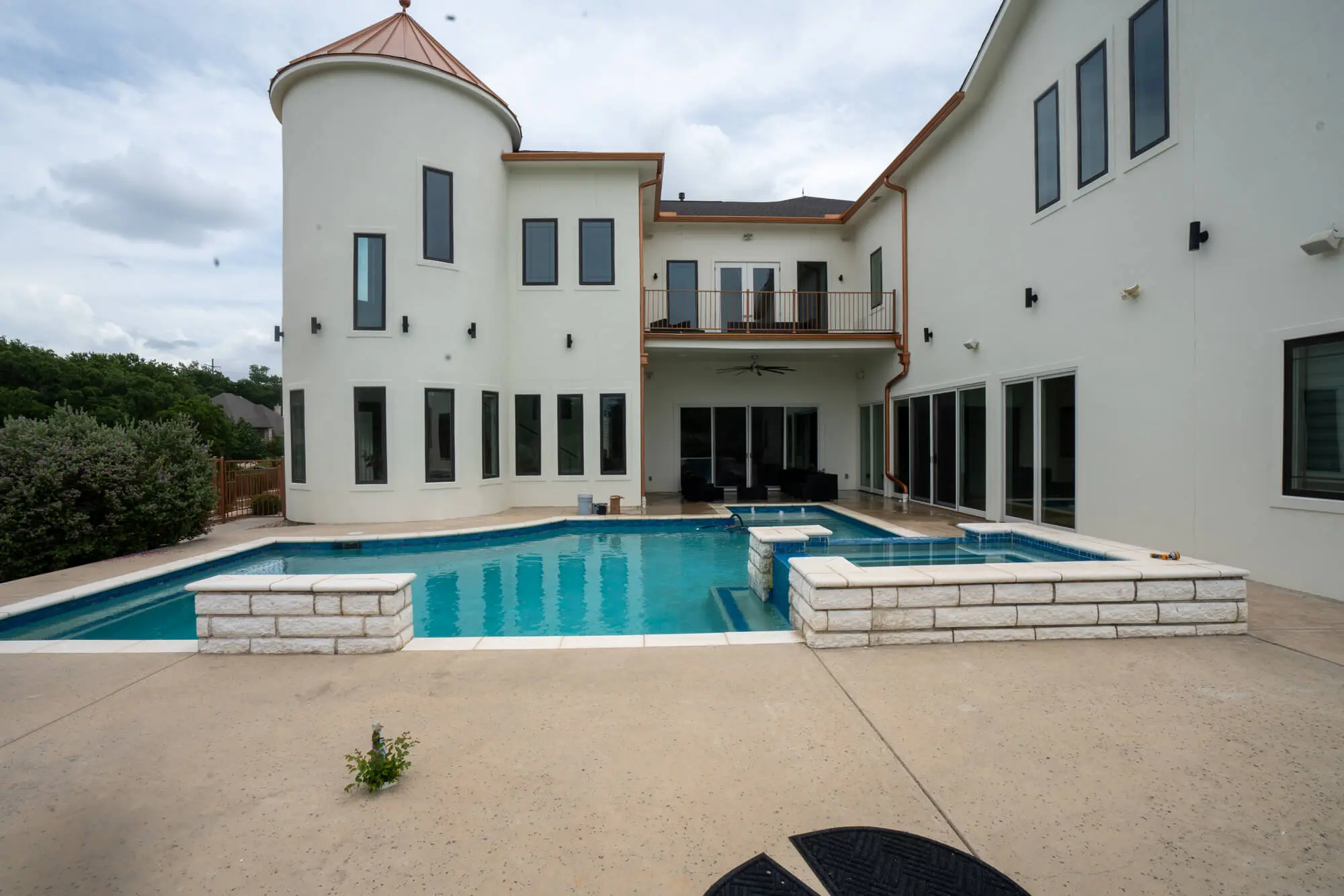 Wide backyard view of a fully completed white stucco exterior repaint on a large DFW estate home with turret tower, copper roofline, second floor balcony, and pool
