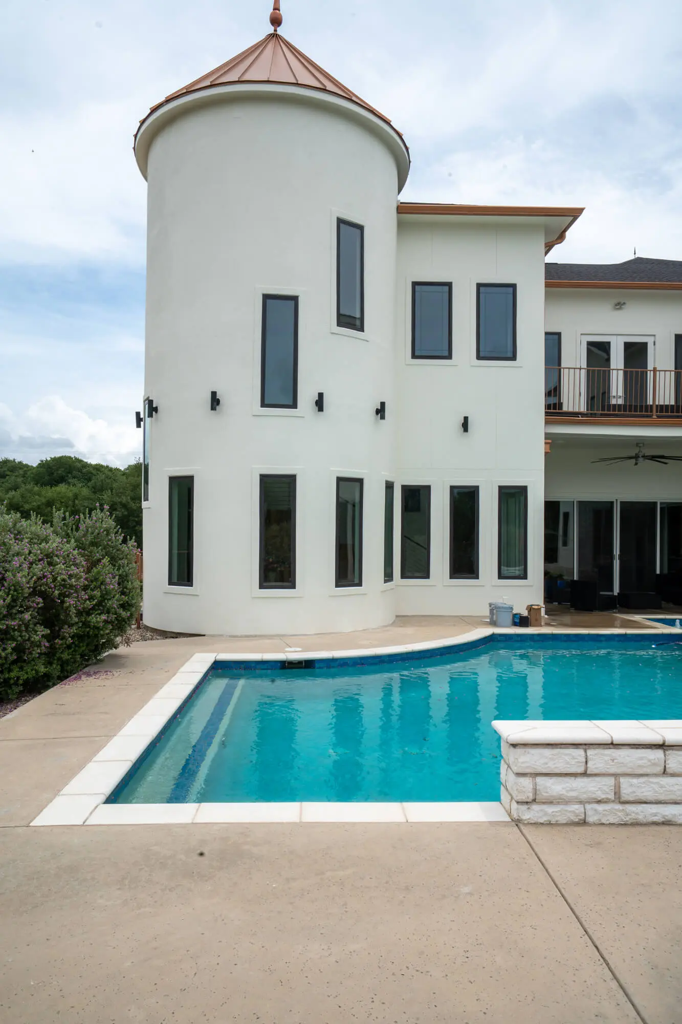 Poolside view of a completed white stucco exterior repaint on a large DFW custom home featuring a round turret with copper cap, charcoal window trim, and second floor balcony