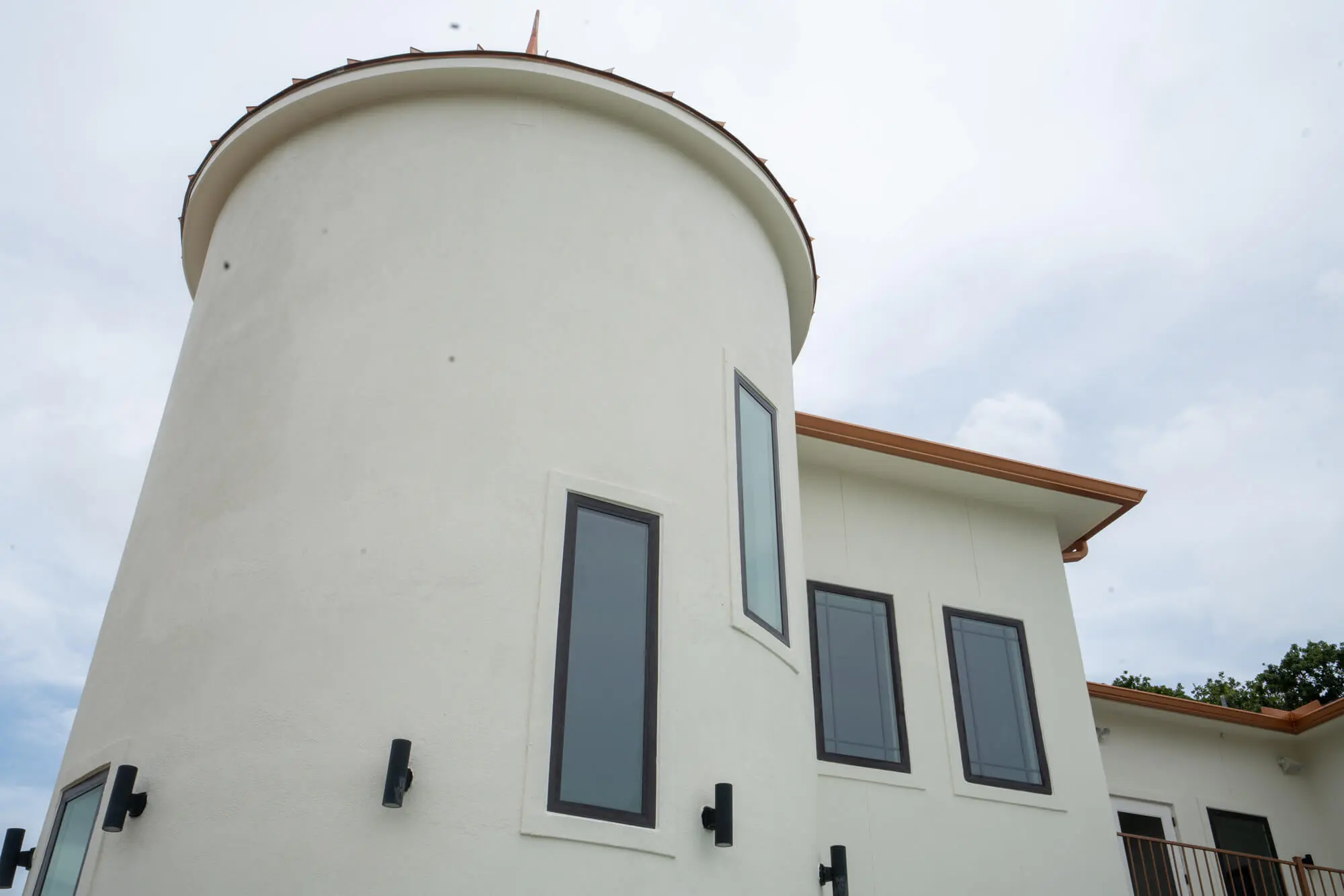 Detailed view of a smooth cream stucco round turret tower with copper roofline cap and charcoal window trim on a completed DFW custom home exterior repaint