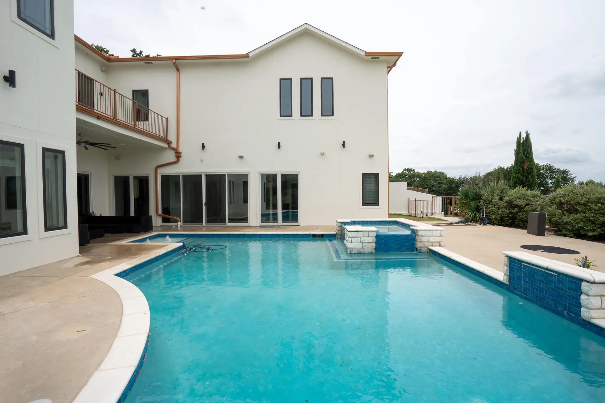 Pool-facing backyard view of a completed white stucco exterior repaint on a large DFW custom home with copper gutters, charcoal trim, and a second floor balcony