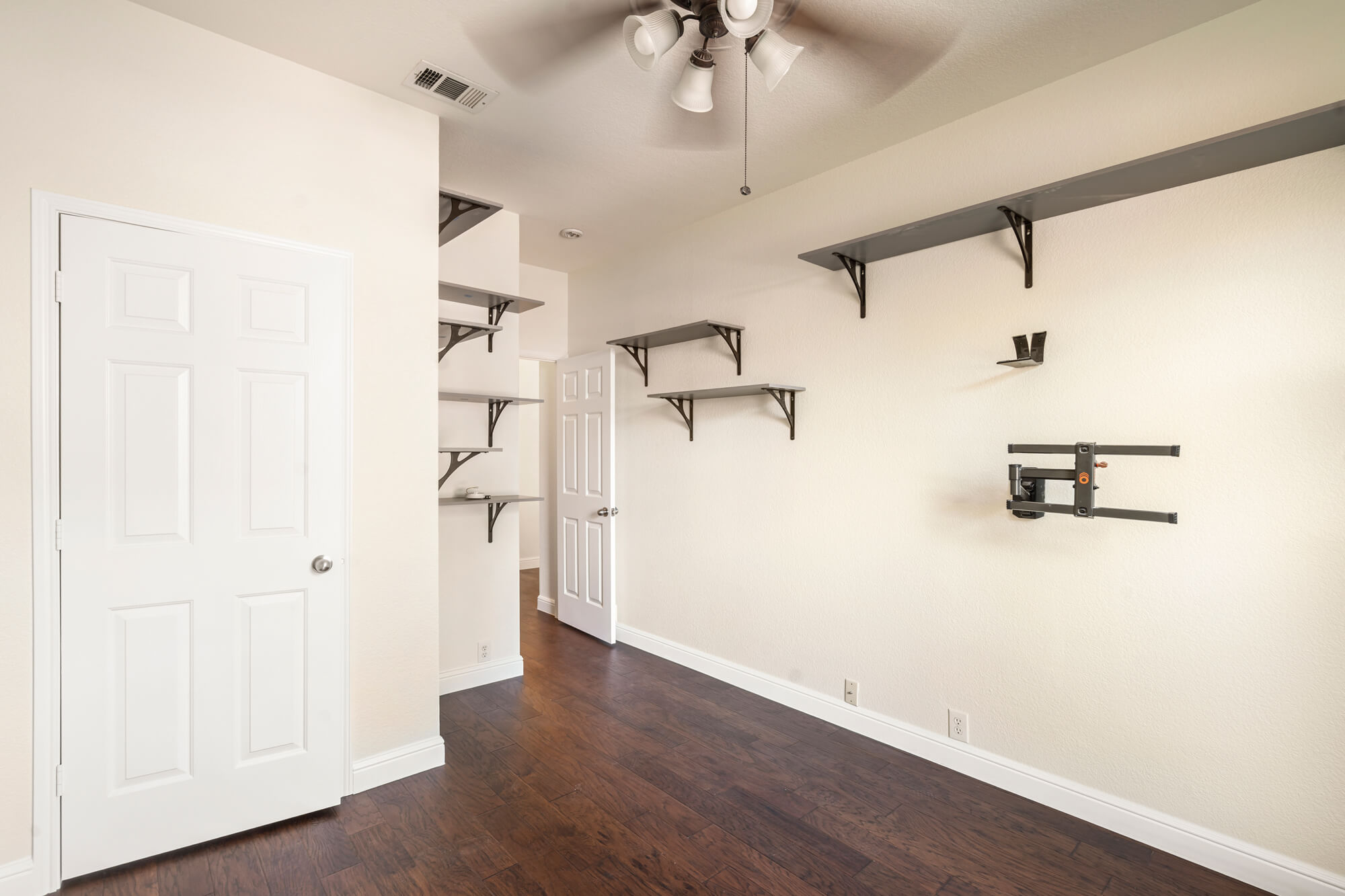 Freshly painted cream bedroom with white doors, white baseboards, dark hardwood floors, and wall mounted shelving completed on a DFW interior painting project by J&R Alliance Painting LLC