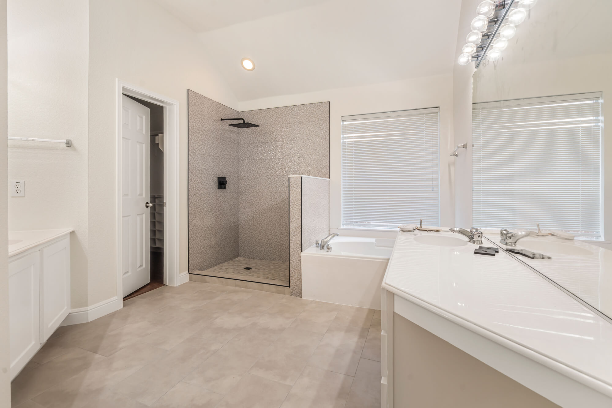 Spacious master bathroom with freshly painted white walls, white vanity cabinet, soaking tub, and open tile shower completed on a DFW interior painting project by J&R Alliance Painting LLC