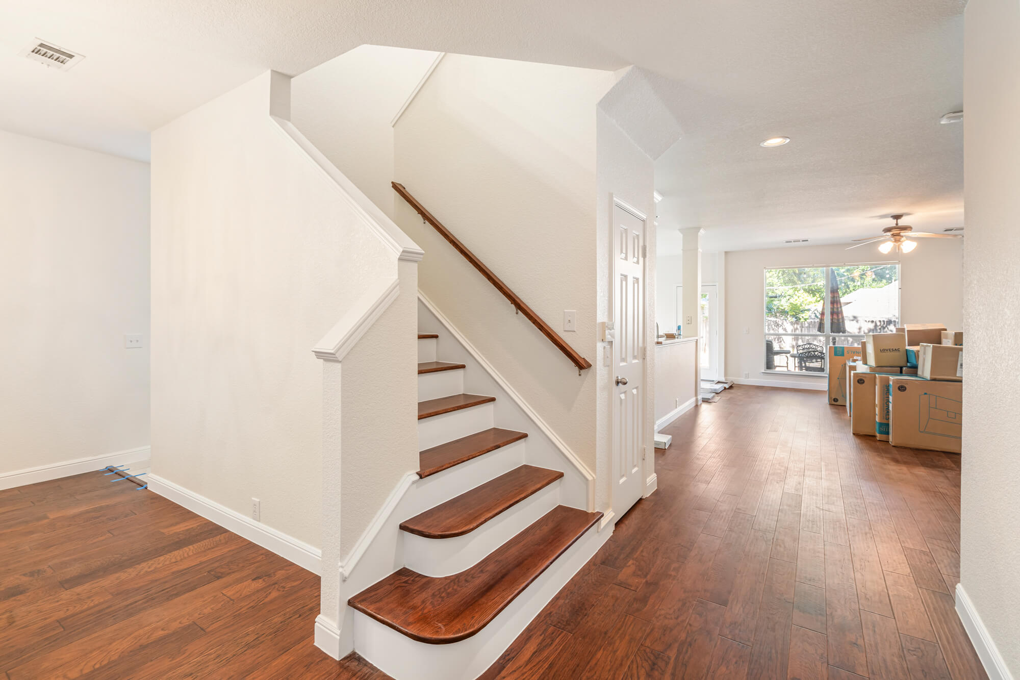 Freshly painted white staircase with wood stair treads, white risers and trim, leading into an open living area with dark hardwood floors on a DFW interior painting project by J&R Alliance Painting LLC