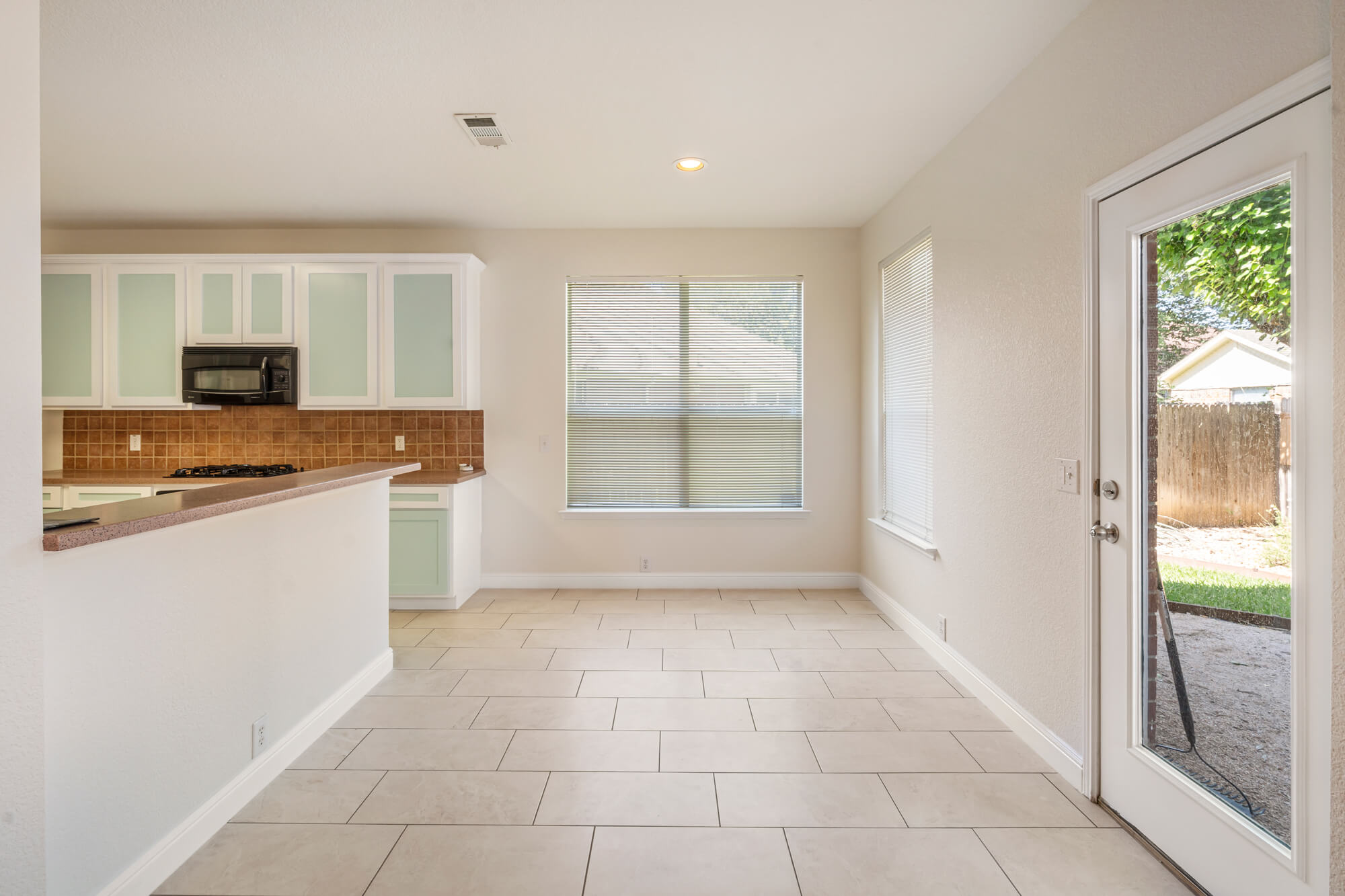 Breakfast nook and kitchen area with freshly painted cream walls, white baseboards, mint green and white refinished cabinets, and tile floors on a cabinet refinishing Fort Worth project by J&R Alliance Painting LLC