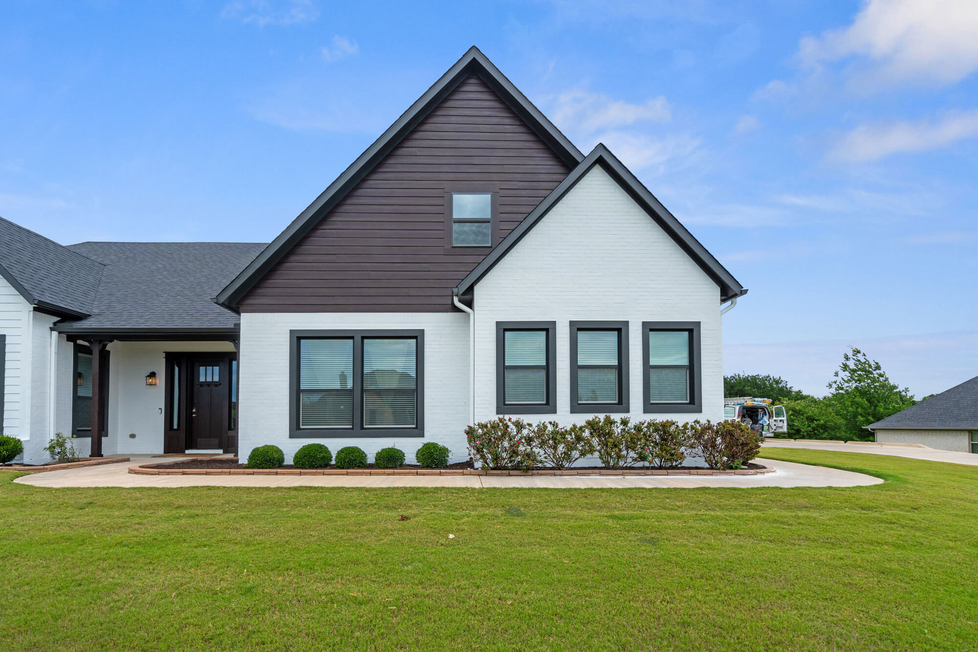 Front elevation of a completed DFW residential exterior repaint with white painted brick, dark brown Hardie siding gable, charcoal window trim, and dark entry door by J&R Alliance Painting LLC