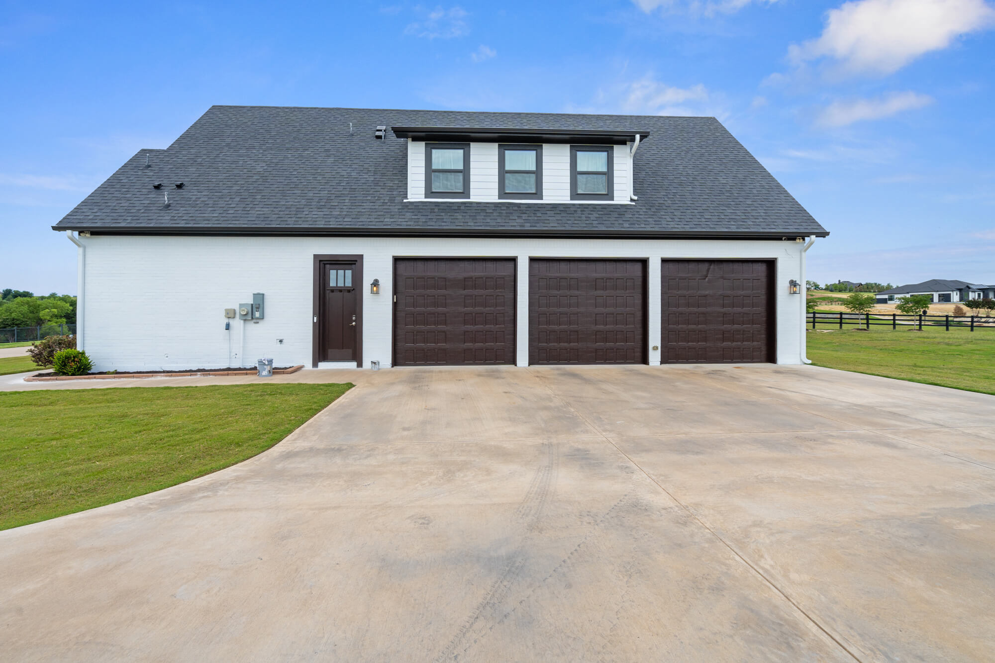 Three car garage elevation of a completed white painted brick exterior repaint with dark brown doors and dormer windows on a DFW residential property by J&R Alliance Painting LLC