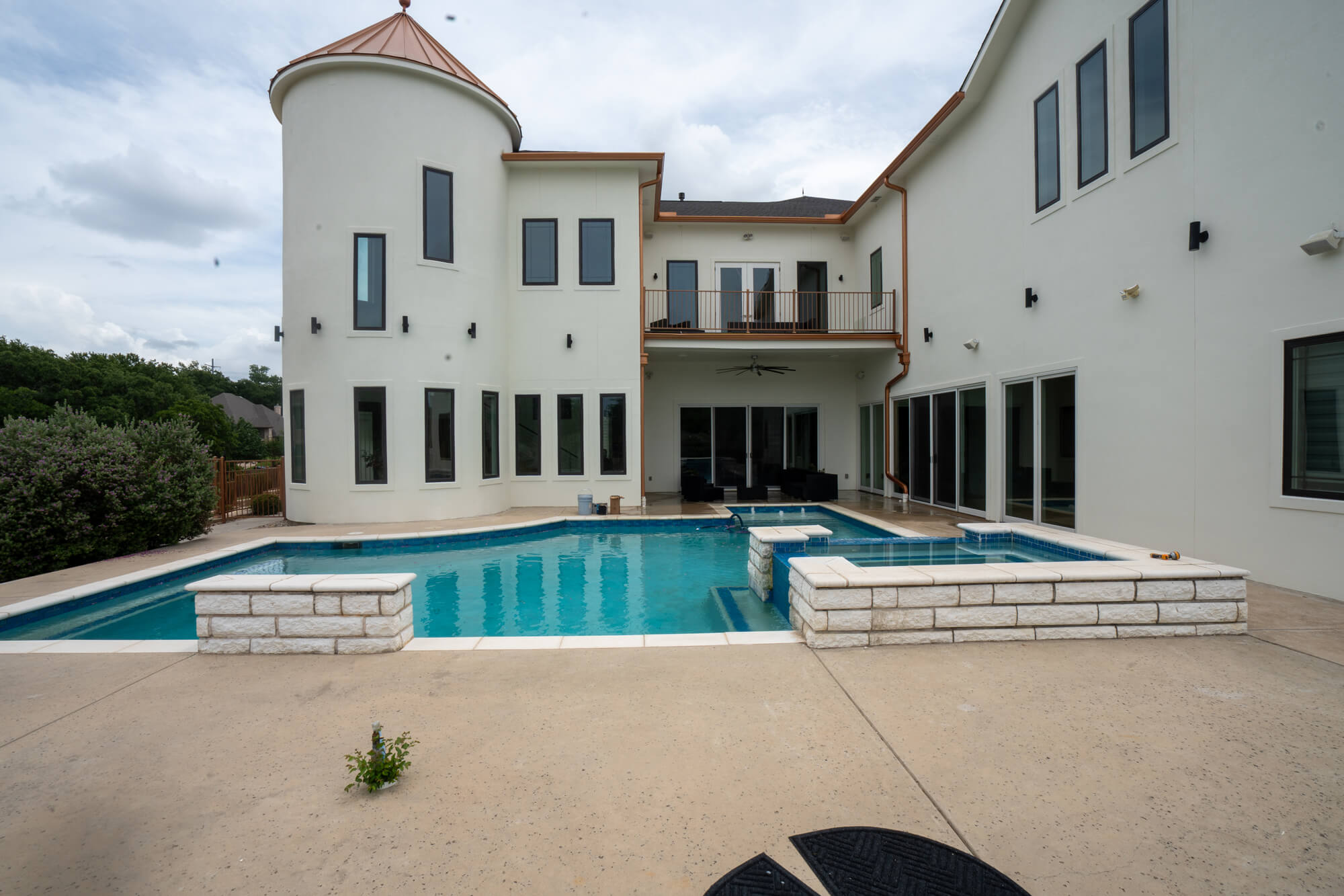 Wide backyard view of a fully completed white stucco exterior repaint on a large DFW estate home with turret tower, copper roofline, second floor balcony, and pool