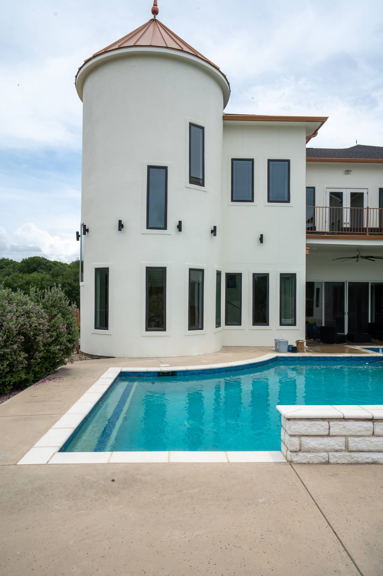 Poolside view of a completed white stucco exterior repaint on a large DFW custom home featuring a round turret with copper cap, charcoal window trim, and second floor balcony