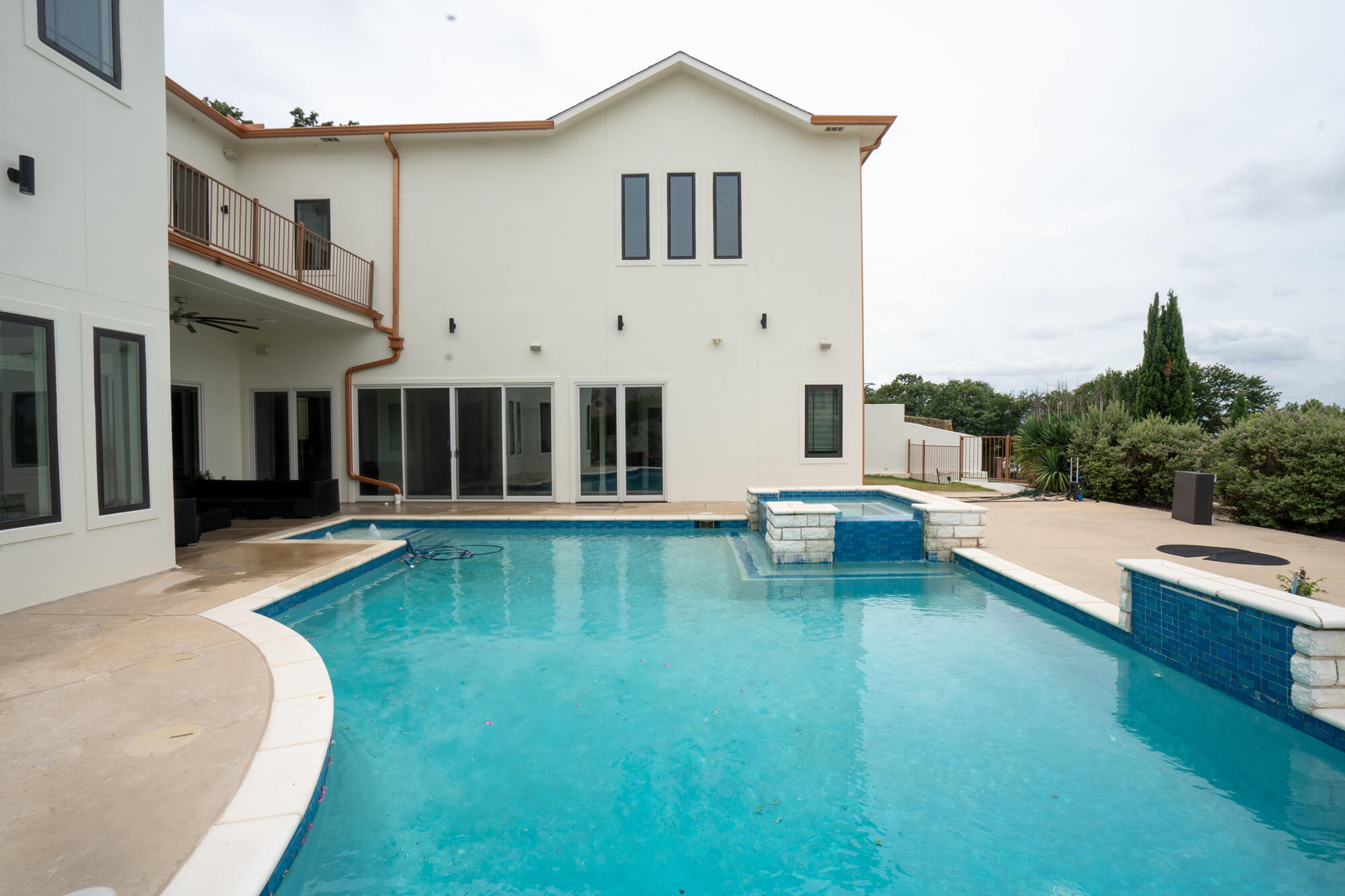 Pool-facing backyard view of a completed white stucco exterior repaint on a large DFW custom home with copper gutters, charcoal trim, and a second floor balcony