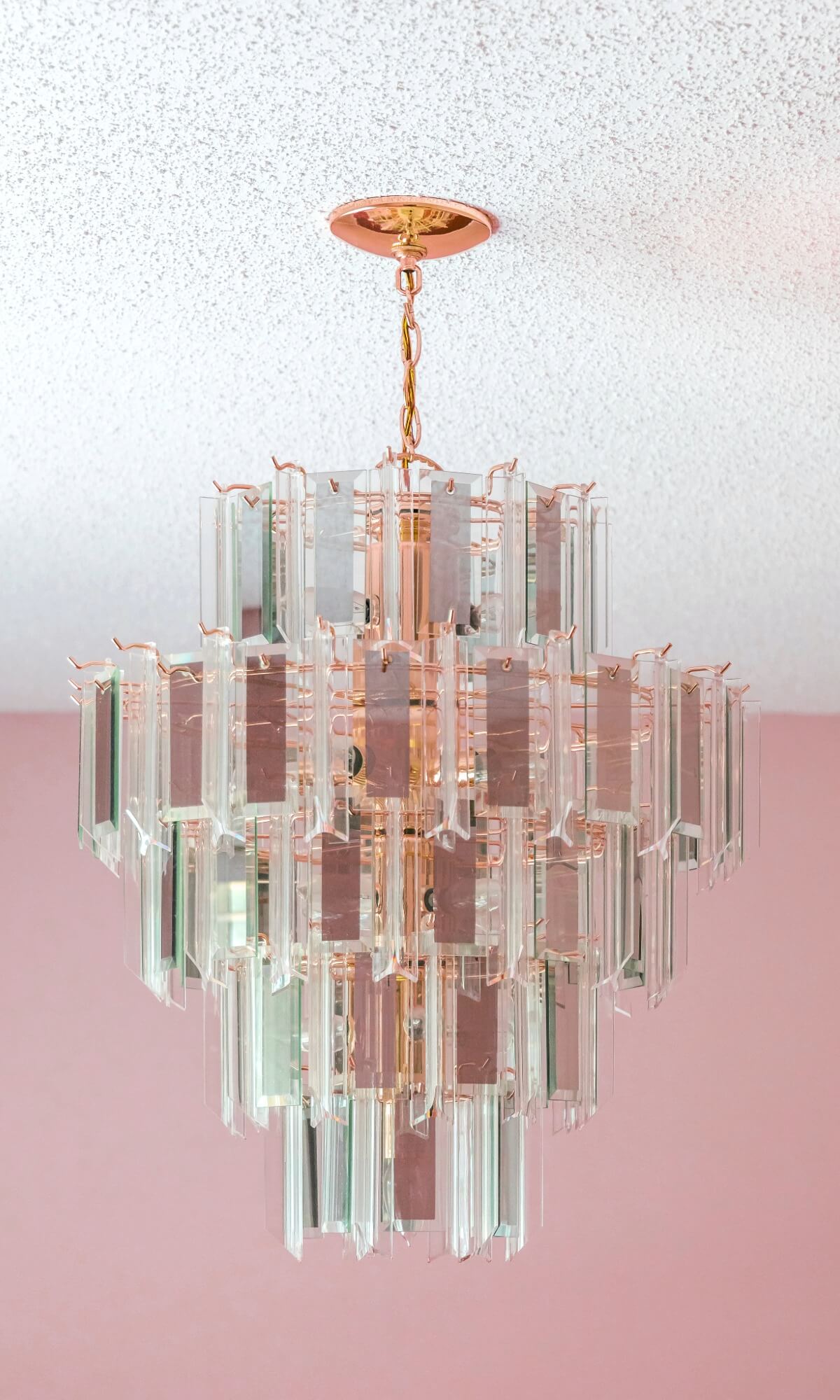 Crystal tiered chandelier hanging from a popcorn texture ceiling with pink painted walls below