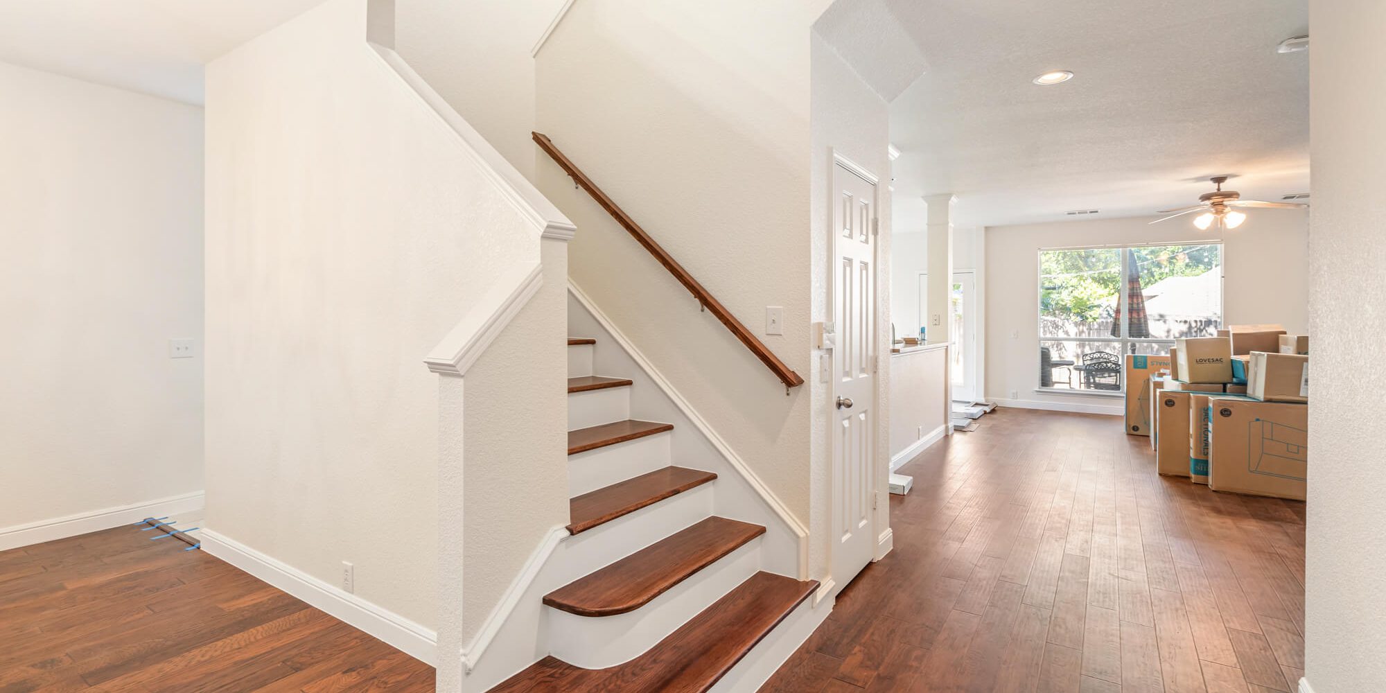 Freshly painted white staircase with wood stair treads, white risers and trim, leading into an open living area with dark hardwood floors on a DFW interior painting project by J&R Alliance Painting LLC