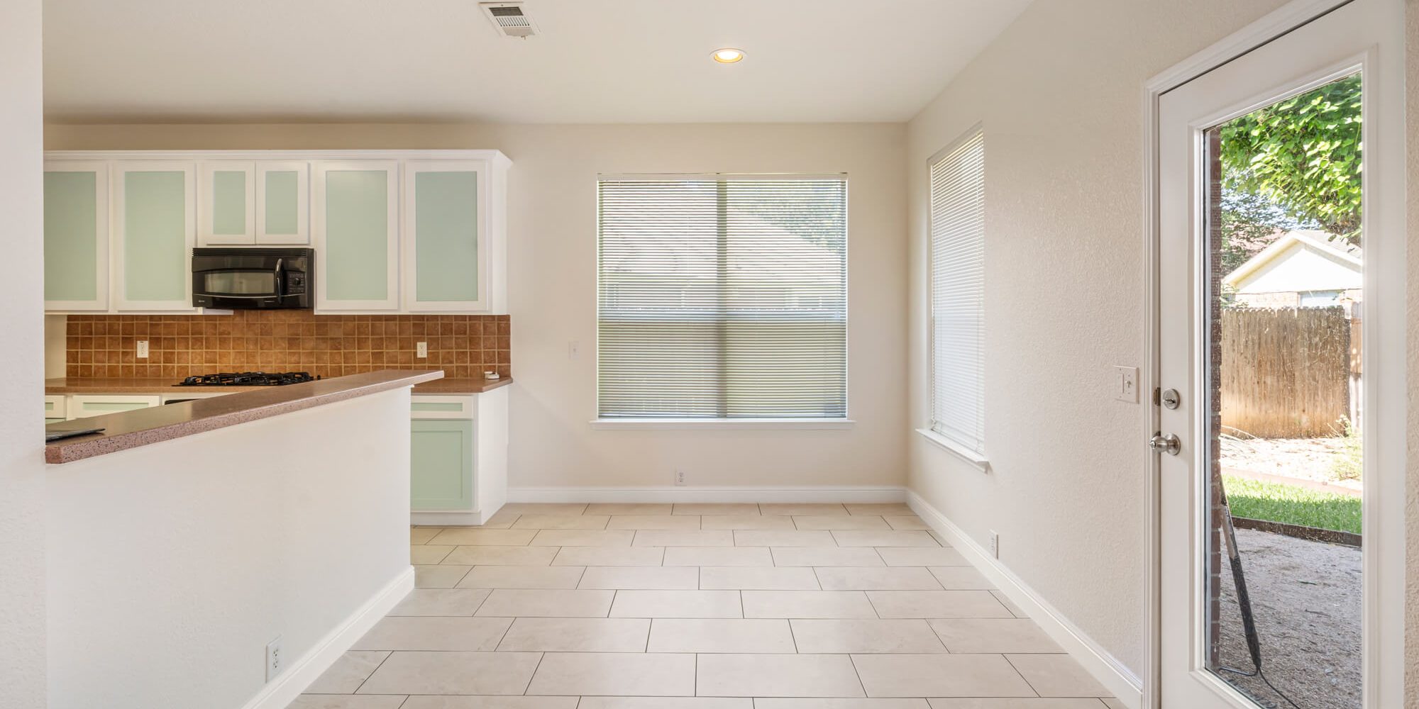 Breakfast nook and kitchen area with freshly painted cream walls, white baseboards, mint green and white refinished cabinets, and tile floors on a cabinet refinishing Fort Worth project by J&R Alliance Painting LLC