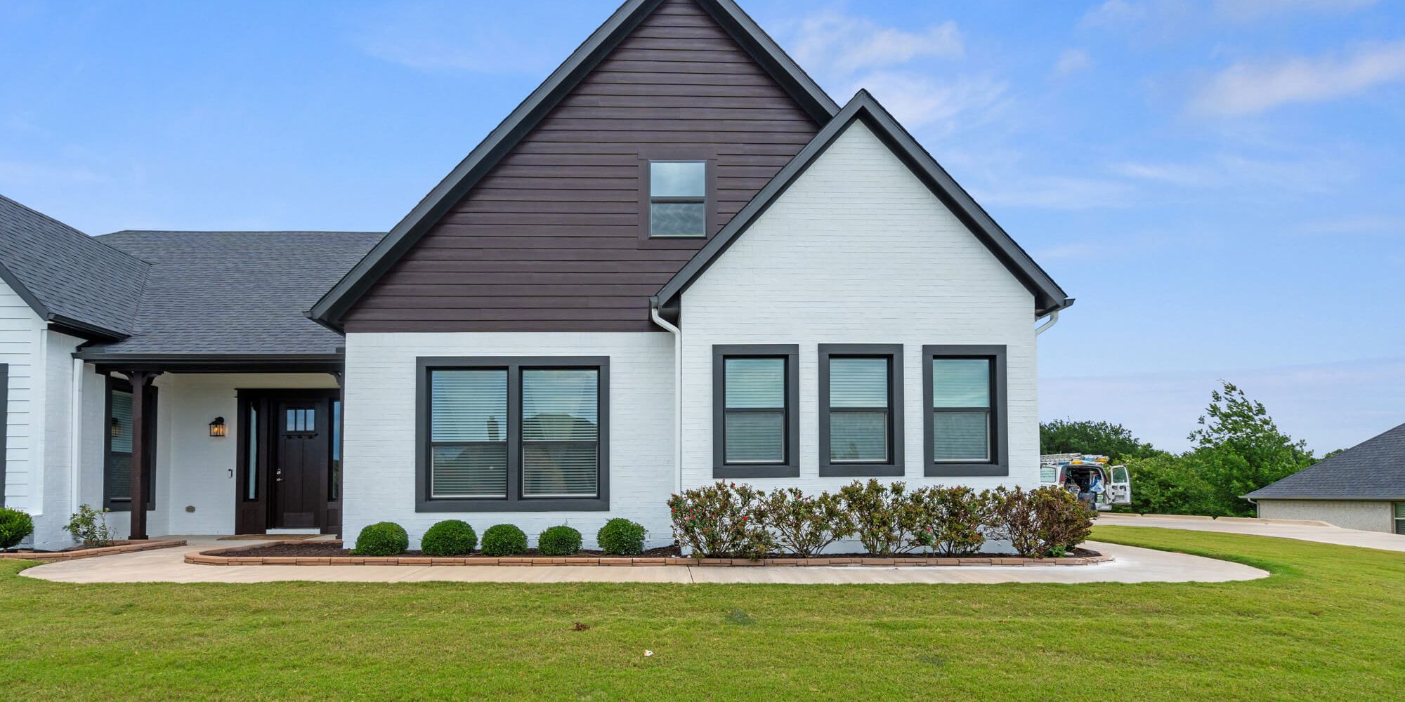 Front elevation of a completed DFW residential exterior repaint with white painted brick, dark brown Hardie siding gable, charcoal window trim, and dark entry door by J&R Alliance Painting LLC