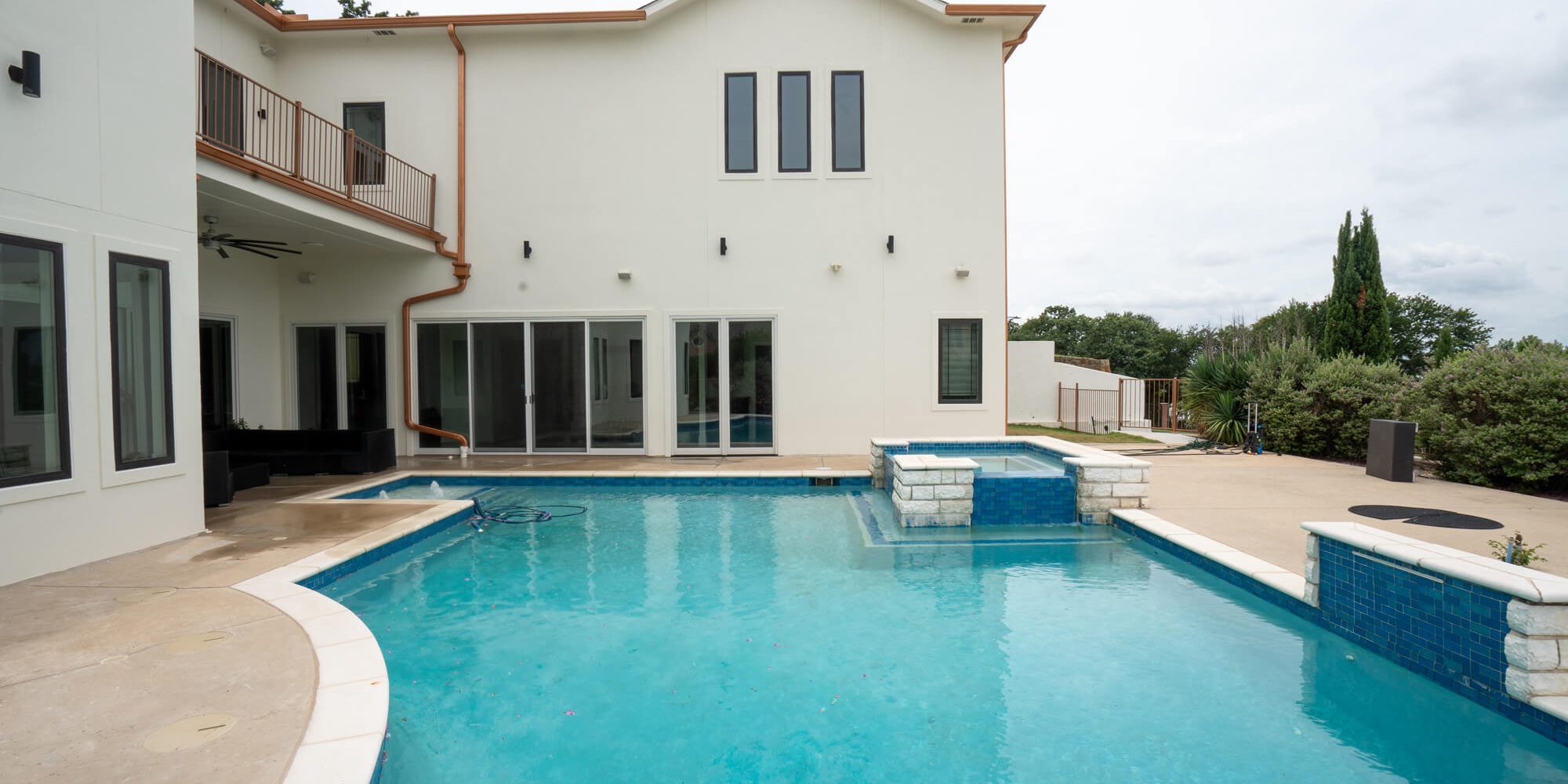 Pool-facing backyard view of a completed white stucco exterior repaint on a large DFW custom home with copper gutters, charcoal trim, and a second floor balcony